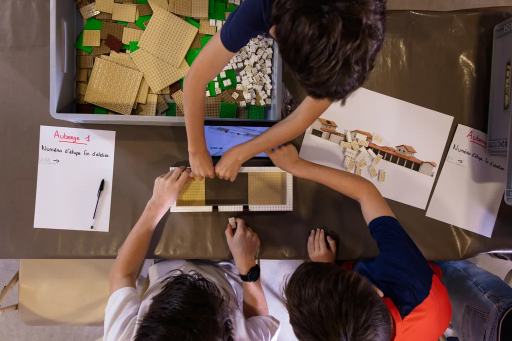 Vue de dessus de la table de montage : le plan imprimé, les bacs de pièces et les mains des participants