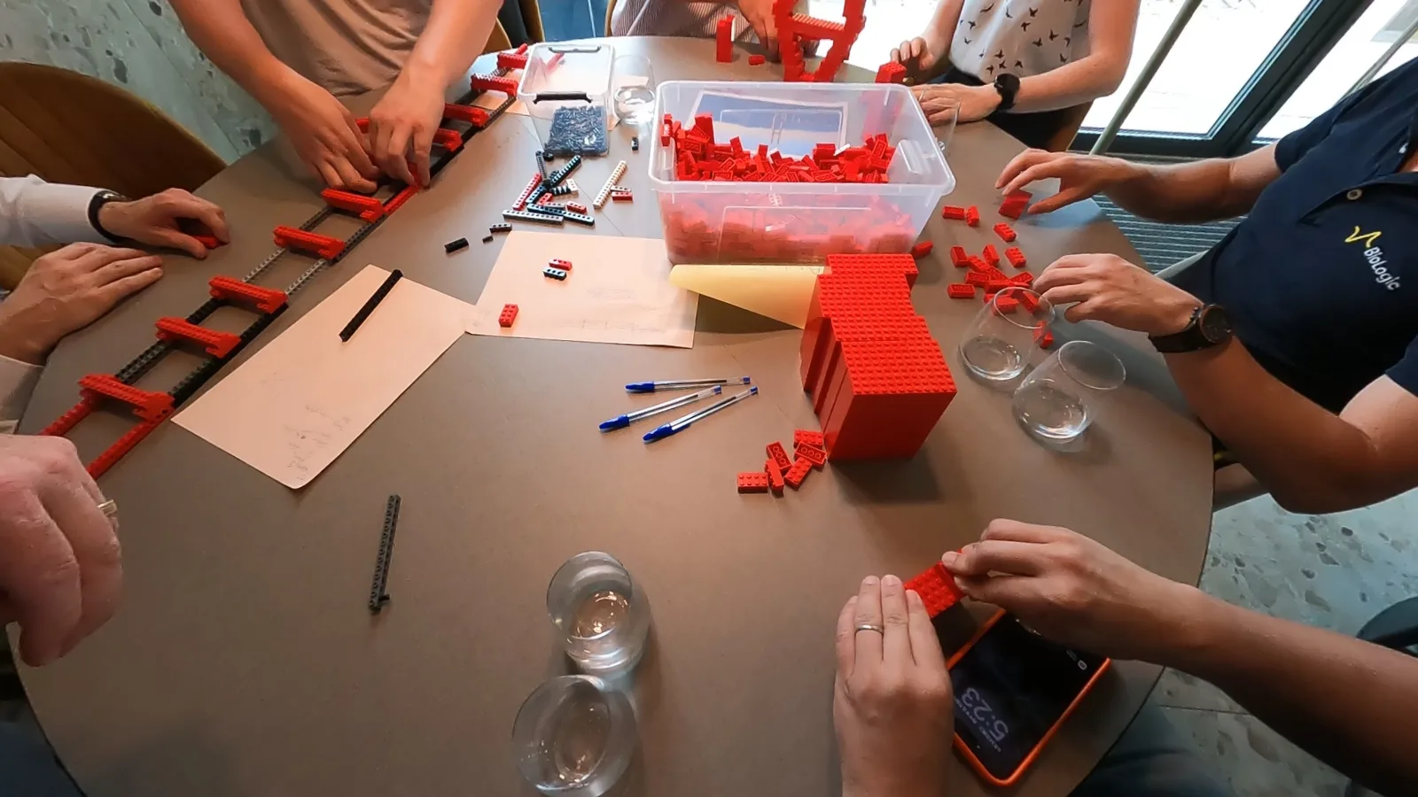 Overhead view of a workshop table: several participants assembling red elements